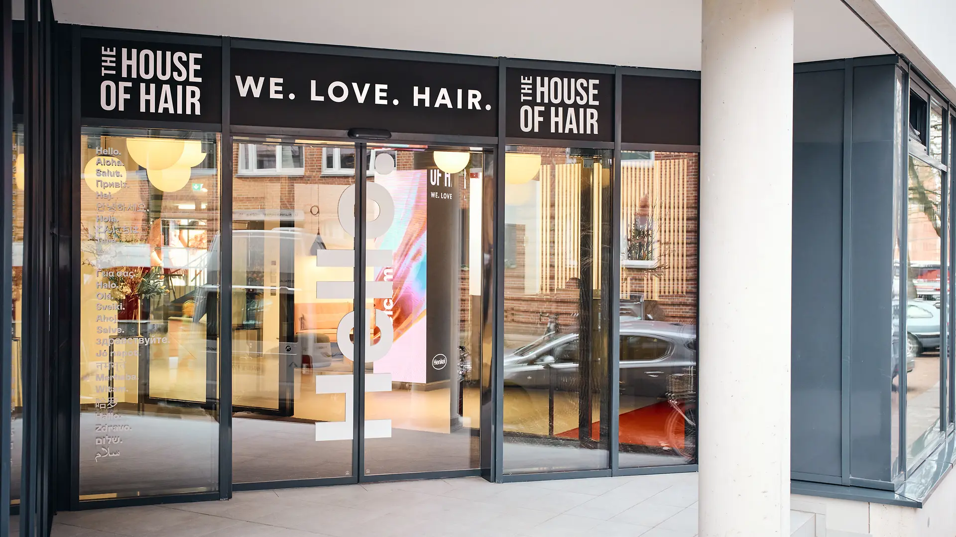 مدخل زجاجي للمركز، وفوق الباب شعار “We. Love. Hair.” وعلى الجانبين عبارة “The House of Hair”.
